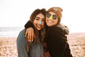 Two smiling friends on a sunny beach wearing Nöz’s natural reef safe sunscreen on their noses